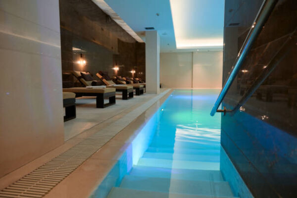 Pool and Spa Lighting Services View of the modern luxurious interior of the spa and wellness center with sun loungers by the thermal pool with underwater lighting and a waterfall.